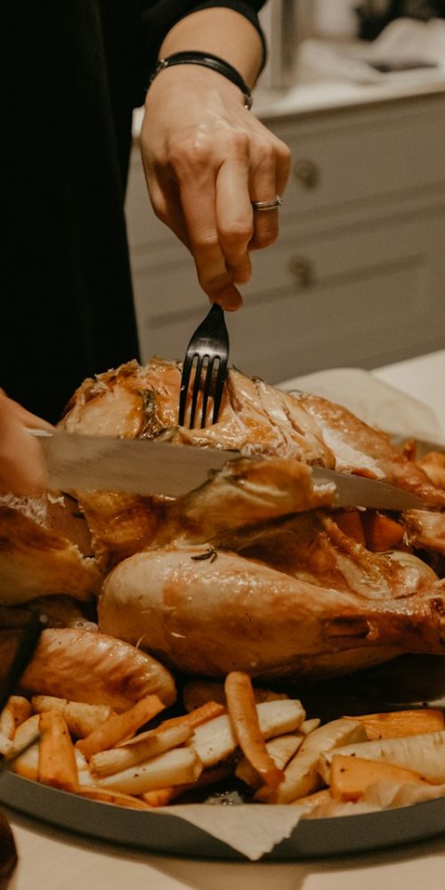 person holding stainless steel fork and bread knife slicing grilled meat on white ceramic plate